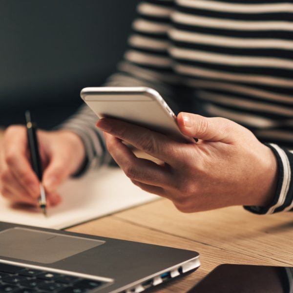 Woman writing contact list from phone into business agenda